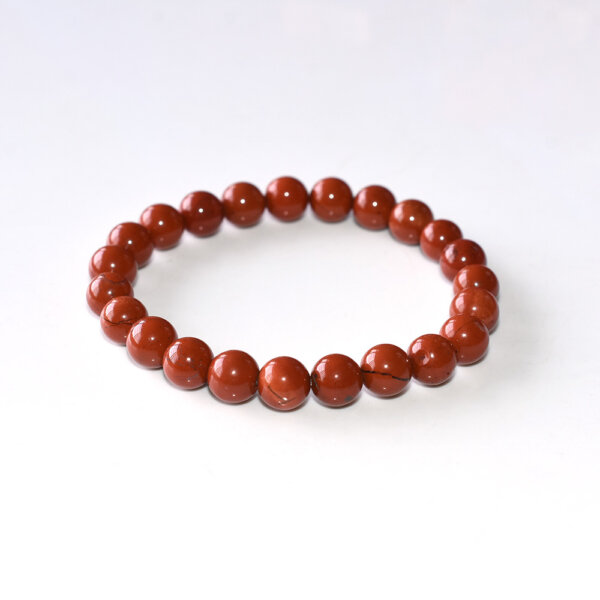 Red Jasper bracelet with polished round beads on white background, handcrafted for grounding energy and natural style.