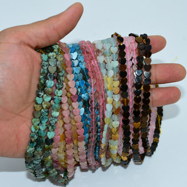 Hand holding multiple strands of 6*6mm heart shaped bead in assorted gemstone colors
