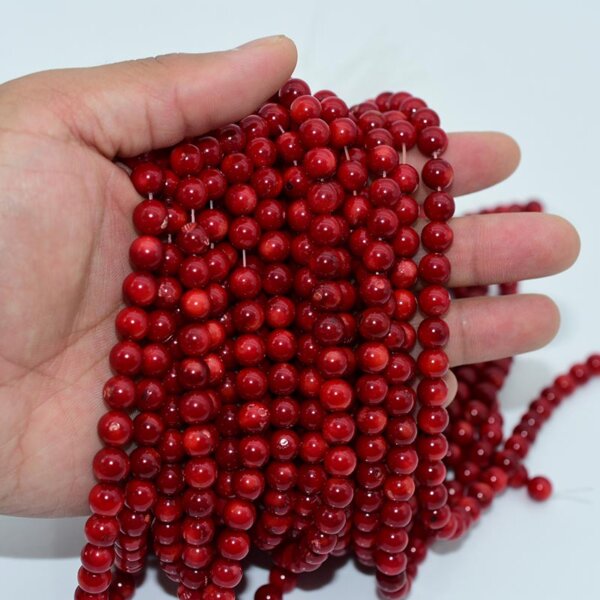 Hand holding multiple strands of polished red coral beads