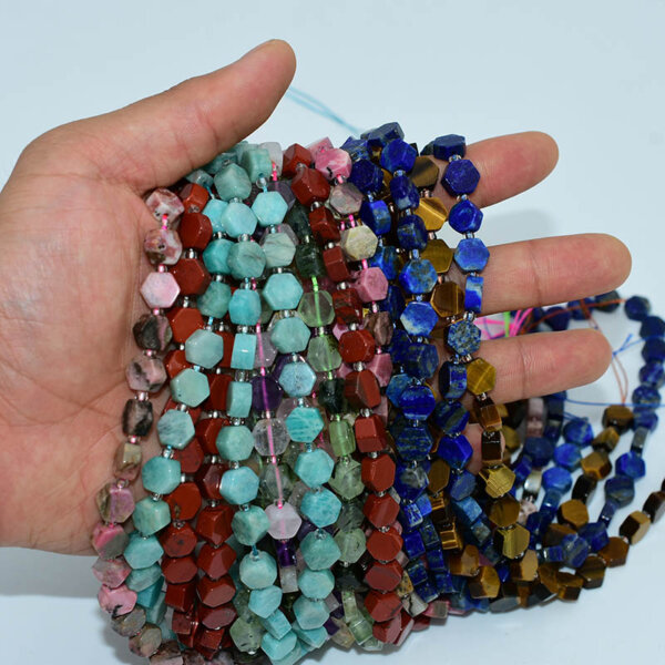 Hand holding assorted hexagon gemstone beads in various colors