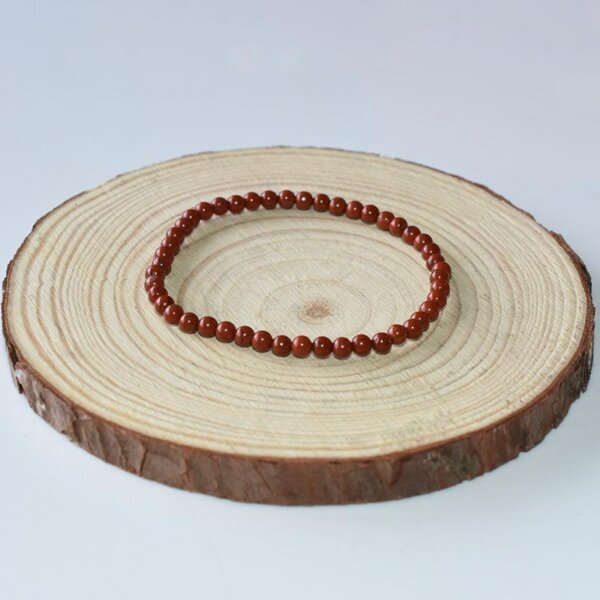 Natural Red Jasper bracelet with small round beads, laid on light wood display.