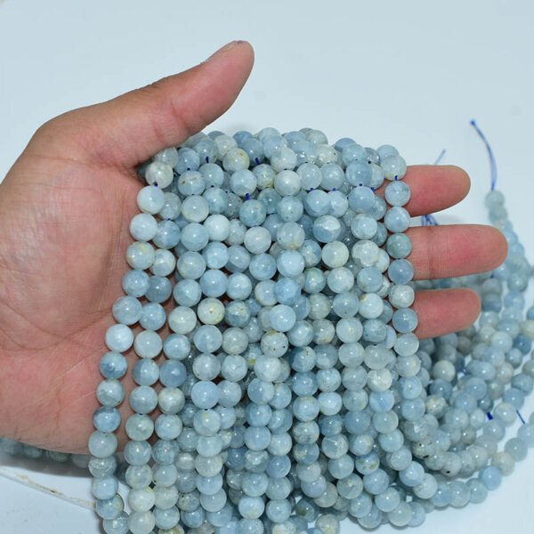 Hand holding celestite beads strand, showing smooth polished blue beads