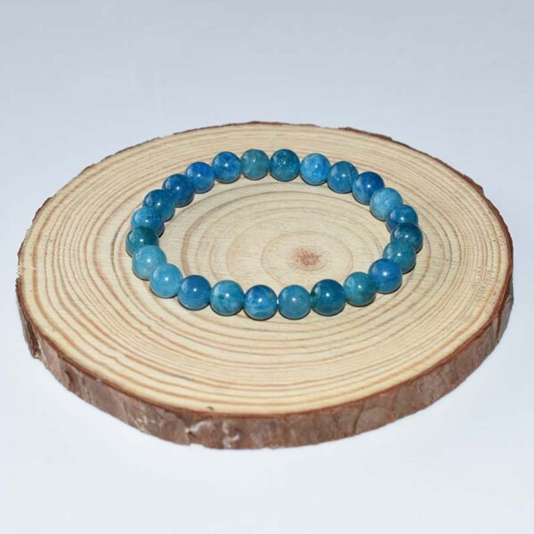 Natural Blue Apatite Bracelet shown coiled on wood slice, emphasizing smooth finish and vibrant color