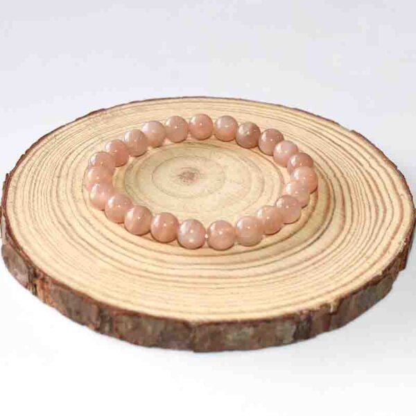 Small-size Sunstone Crystal Bracelet with uniform peach beads, laid on natural wood slice