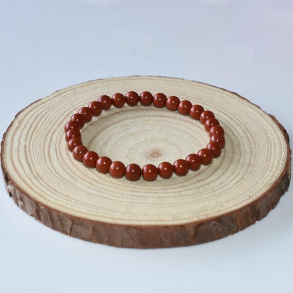 Natural Red Jasper bracelet with small round beads, laid on light wood display.