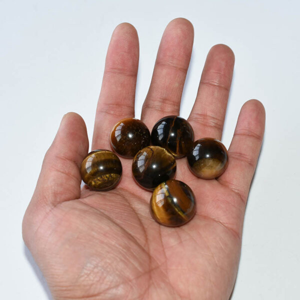 Hand holding polished Tiger Eye Spheres of mixed sizes for scale reference