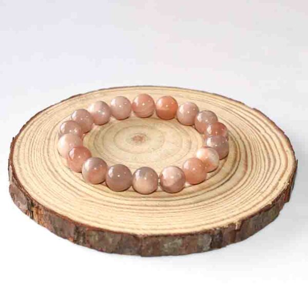Round Sunstone Beaded Bracelet arranged in a circle on wood slab, peach-colored gemstone accessor