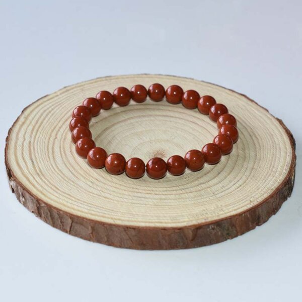 Red Jasper bracelet with medium-sized beads, neatly arranged in circle on wood background.