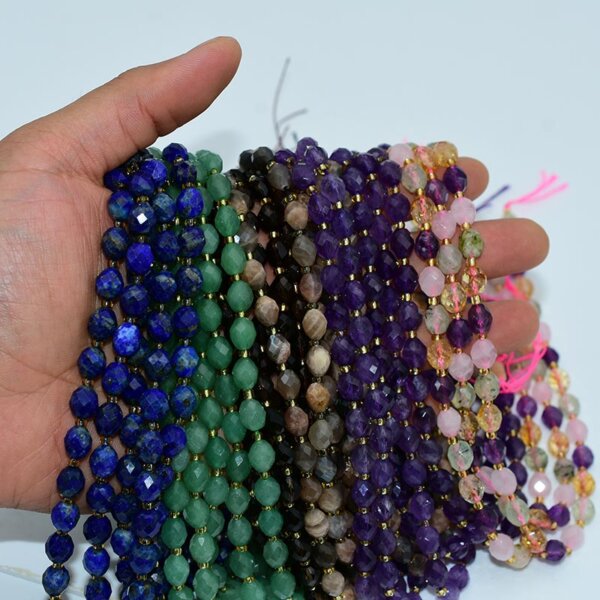 Hand holding assorted faceted rice beads strands in lapis lazuli, green aventurine, amethyst, and other crystals