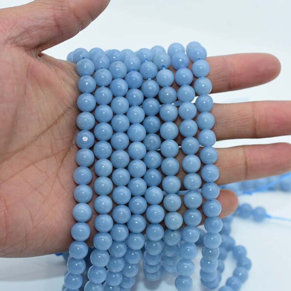 Hand holding multiple strands of Angelite Beads in soft blue tone
