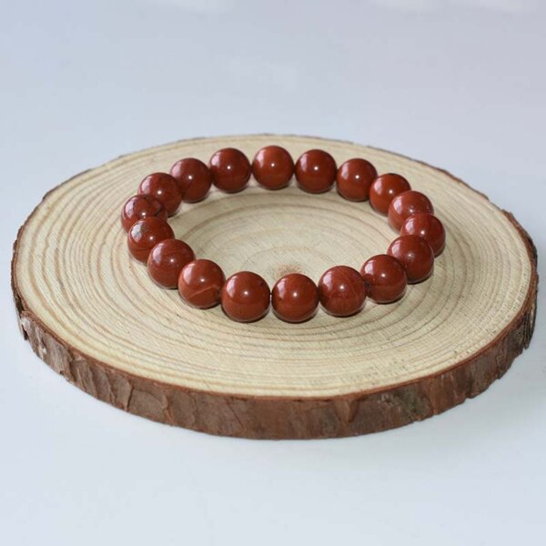 Single strand Red Jasper bracelet displayed on wooden base, featuring polished round beads.