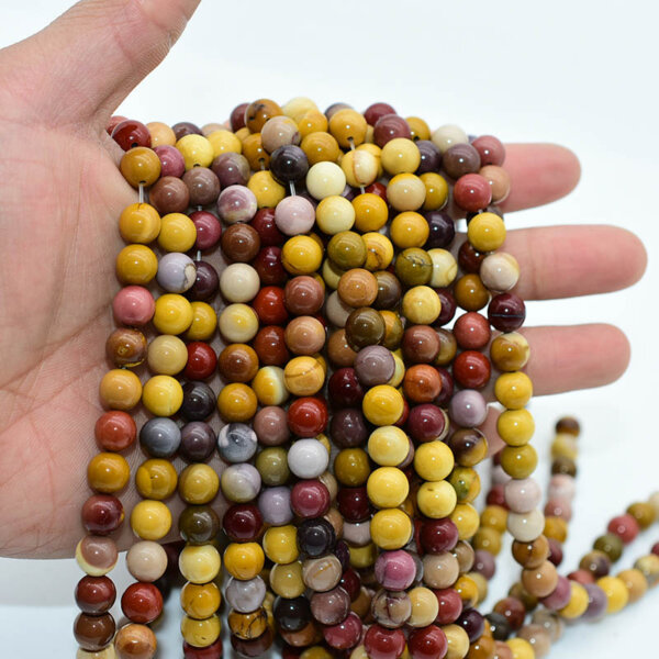 Hand holding strands of polished Mookaite Jasper beads in mixed earth tones
