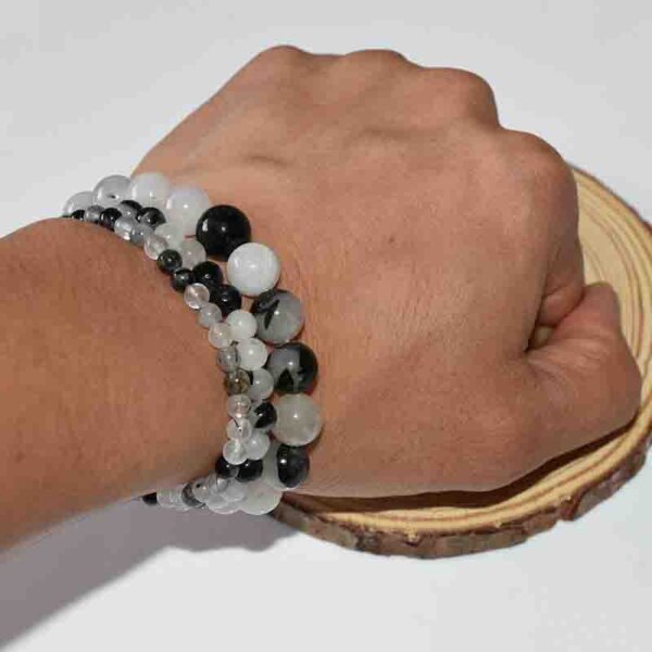 Hand wearing Black Rutilated Quartz bracelet displayed with natural wooden slice