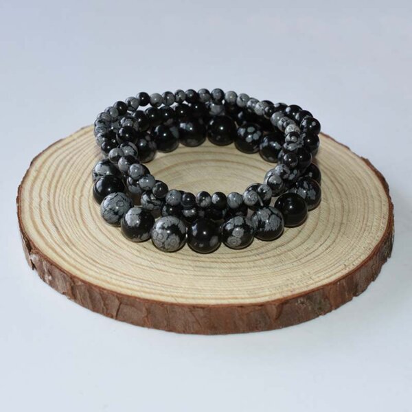Multiple Snowflake Obsidian bracelets coiled on wooden display, featuring polished black beads with white snowflake patterns.