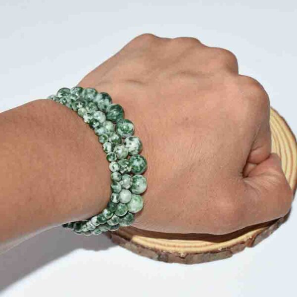 Hand wearing Green Spot Jasper bracelet with natural wooden display base