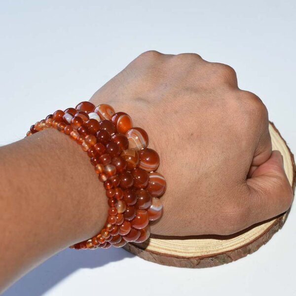 Hand wearing stacked carnelian bracelets, showing natural red-orange shine