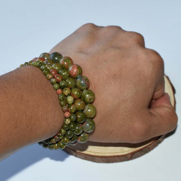 Hand wearing multiple layered Unakite Bracelets showing natural red and green stone patterns.