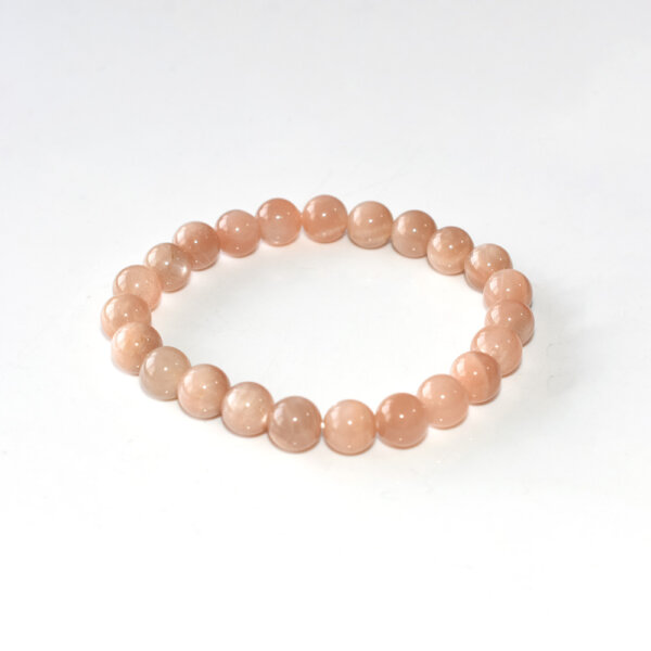 Sunstone Crystal Bracelet with round peach-colored beads on white background, minimalist flat lay