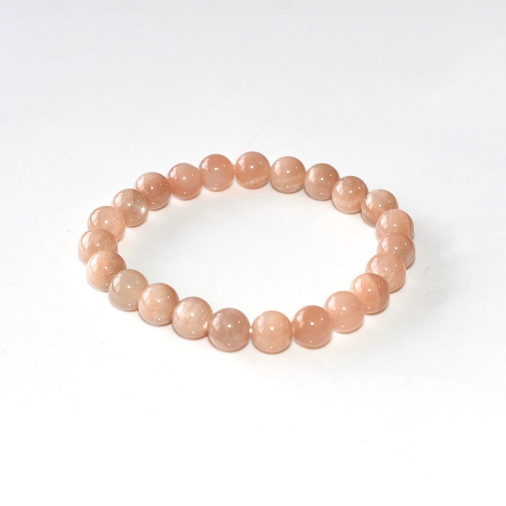 Sunstone Crystal Bracelet with round peach-colored beads on white background, minimalist flat lay