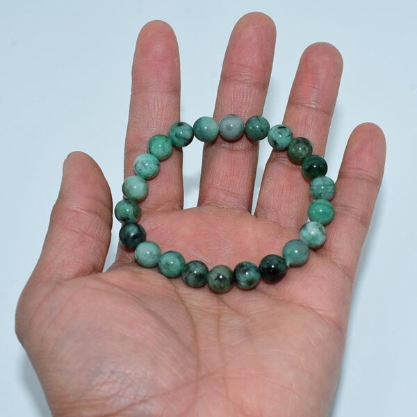 Hand holding emerald bracelet to highlight bead size and color