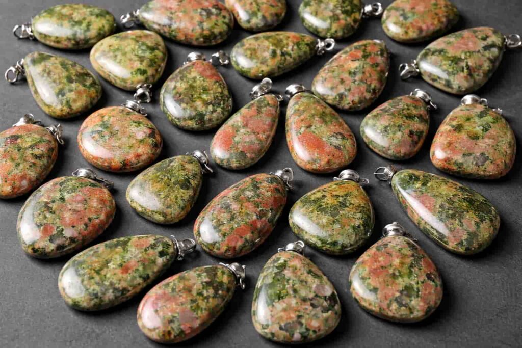 Multiple polished Unakite Jasper pendants featuring green and pink patterns, arranged on a dark background, highlighting their natural beauty and reflecting Unakite Meaning related to emotional balance and healing.