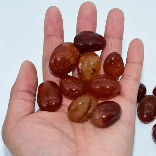 Hand holding multiple Tumbled Carnelian stones, polished 20–30mm size