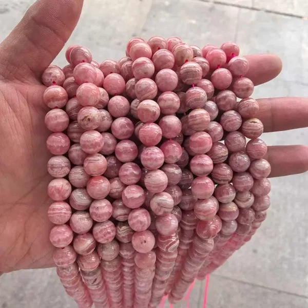 Rhodochrosite Beads 8mm round strands held in hand, natural pink red gemstone