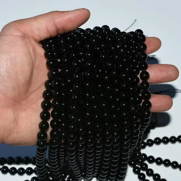 Hand holding multiple strands of Genuine Black Tourmaline Beads