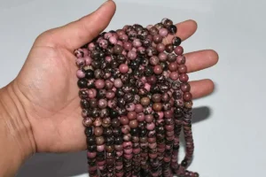 Hand holding multiple strands of Rhodonite Beads with natural pink and black veining