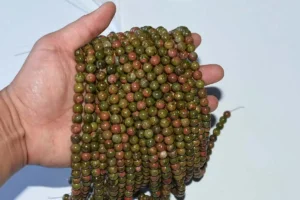 8mm Unakite Beads on hand, showing natural green-pink pattern