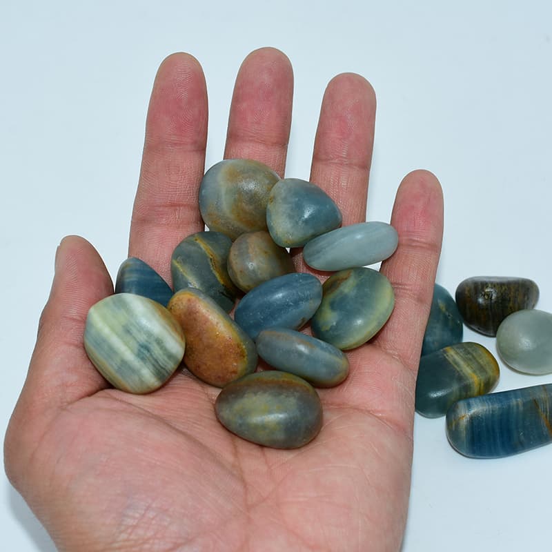 Blue Calcite Tumbled stones resting on palm, showing realistic size and natural color variation.