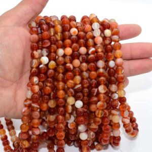 Carnelian Bead strands on hand demonstrating color variation and shine