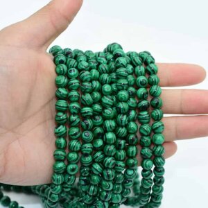 Fake Malachite Beads in hand showing realistic weight and smooth stringing