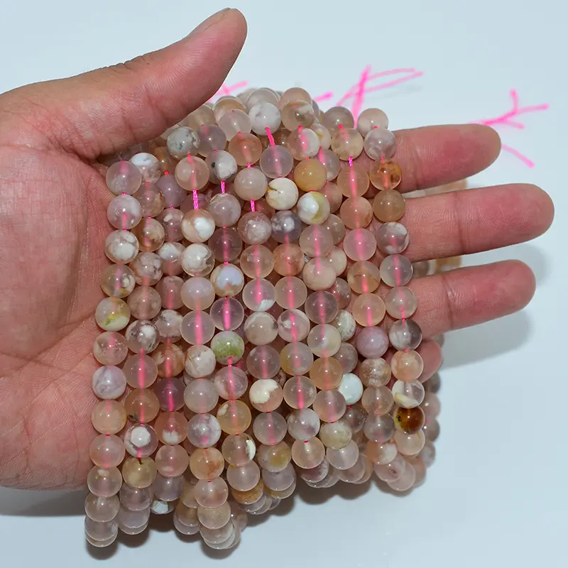 Hand holding strands of natural flower agate beads, emphasizing texture, shine, and authentic gemstone beauty.