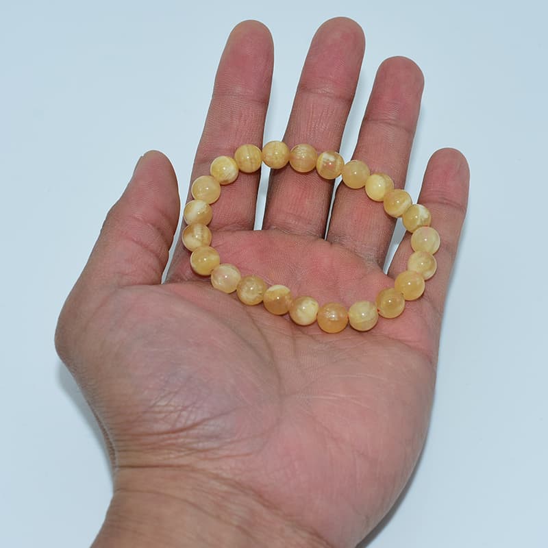 Orange Calcite Bracelet in hand demonstrating clarity, size, and natural light reflection