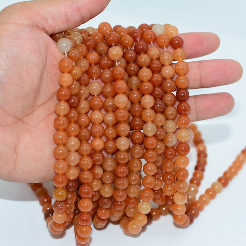 Hand holding Red Aventurine Beads strands to show natural size and luster