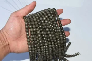 pyrite beads on hand to show size and luster—multiple strands displayed for scale.