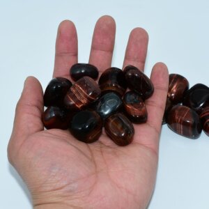 Tumbled Red Tigers Eye in hand to show real-life scale, shape, and sheen