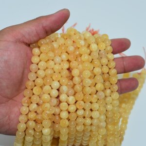 Orange Calcite Beads in hand to show bead size and strand density